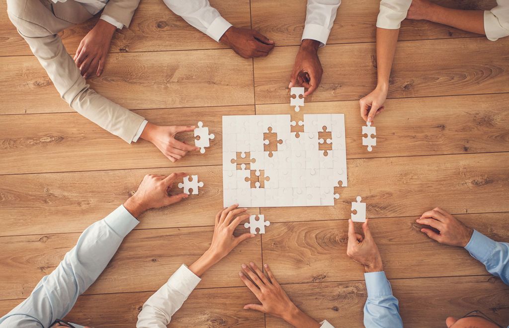 Business people sitting at office desk, putting puzzle pieces together, finding solution