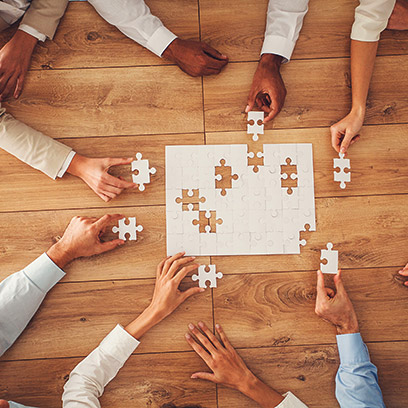 Business people sitting at office desk, putting puzzle pieces together, finding solution